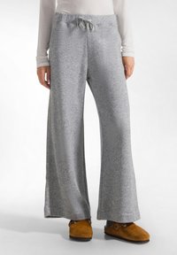 Grijze, wijde sweatpants met een trekkoord in de taille en subtiele glans, gemaakt van zachte stof, gecombineerd met bruine slippers.