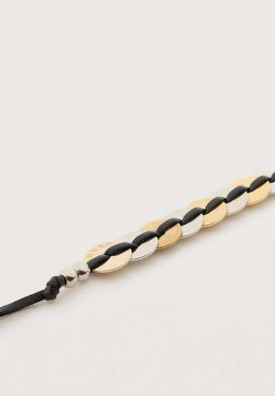 Κοντινό πλάνο βραχιολιού με εναλλασσόμενους χρυσούς και ασημένιους οβάλ μεταλλικούς κρίκους, πλεγμένους με μαύρο κορδόνι.