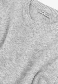 Suéter gris claro hecho de material suave con un cuello redondo acanalado. Presenta una textura delicada y una etiqueta que muestra de manera destacada "DAN JOHN".