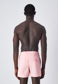 Pantaloni da mare rosa con vita elasticizzata e tasca posteriore, caratterizzati da un tessuto leggero e strutturato e da un taglio moderno.