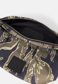 Borsa in tessuto a righe nere e beige con chiusura a zip. L'interno è liscio, scuro, e presenta un'etichetta in pelle con il marchio.