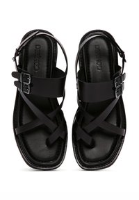 Sandalias negras con tiras entrecruzadas, hebillas ajustables, textura de cuero suave y diseño de punta cuadrada. Estética minimalista y moderna.