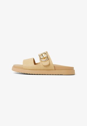 Sandalia deslizante de tono beige claro con un upper texturizado, una correa ancha y un acento de hebilla circular en tono dorado. Presenta una suela de goma plana con estrías.