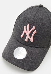 Grå keps med en rosa broderad 'NY'-logotyp på framsidan. Inkluderar en cirkeltagg med "9FORTY" och "KVINNOR". Slät tygtextur.