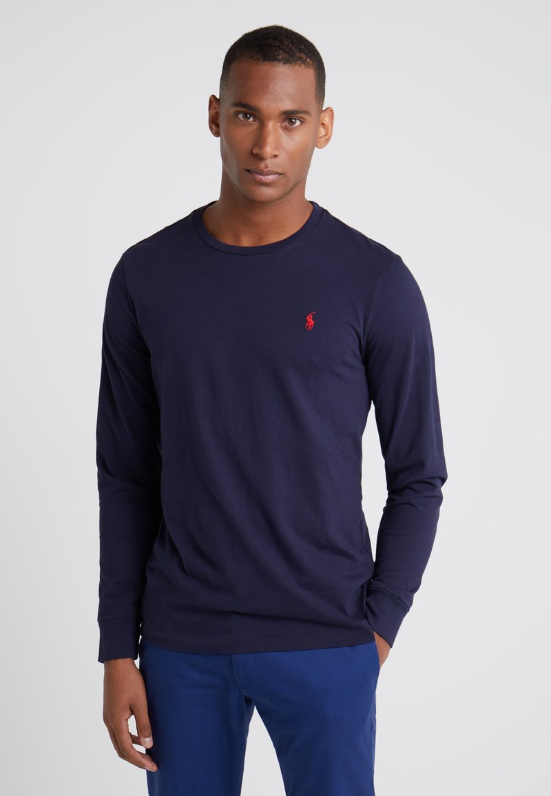 Marineblauw T-shirt met lange mouwen van katoen, met een ronde hals en een klein rood logo op de linkerborst. Soepele textuur en een aansluitend ontwerp.
