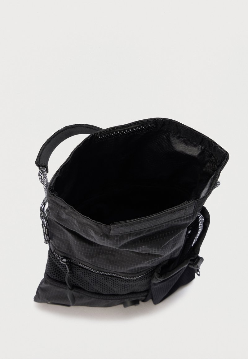 Sacca nera con coulisse dotata di tasca in rete e compartimento con cerniera, mostrata aperta dall'alto su uno sfondo uniforme.