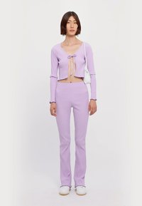 Ribbed lavender crop top with a front tie detail paired with matching flared pants. Smooth texture and fitted silhouette. White footwear shown.