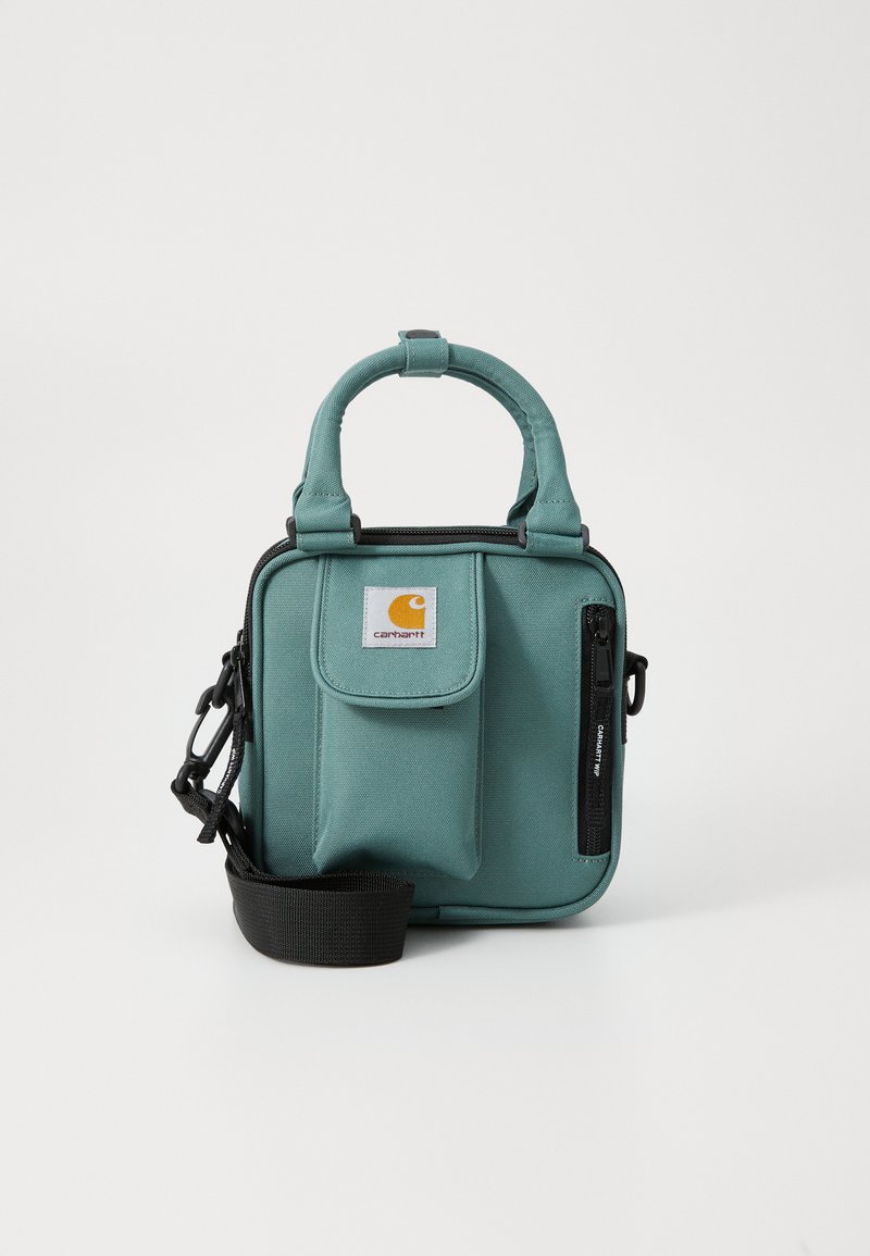 Zelena tkanina torbica preko ramena s kratkim ručkama, zippered džepom, prednjim džepom s preklopom, podesivim remenom i Carhartt logotipom sprijeda.