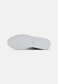 Suola di scarpa in gomma bianca con superficie texturizzata che presenta motivi triangolari e un design piatto, probabilmente per grip e trazione.