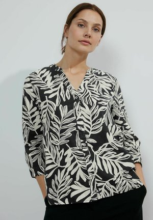 Camicia a bottoni bianca e nera con scollatura a V, caratterizzata da un motivo a foglie, maniche lunghe e una vestibilità rilassata. La texture del tessuto appare leggera.