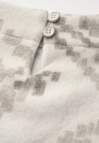 Pullover in hellgrau und weiß gestrickt mit einem dezenten Pixelmuster, ausgestattet mit einer Knopfleiste am Hals mit zwei hellgrauen Knöpfen.