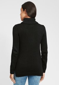 Schwarzer Strickpullover mit einem gerippten Rollkragen, langen Ärmeln und einem etwas längeren Rücken. Die Textur ist dick und gemütlich, ideal zum Schichten.