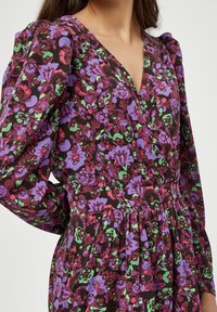 Blumenkleid mit braunem Grundton und lila, rosa und grünen Mustern, V-Ausschnitt, Puffärmeln und gesammeltem Taillendetail.