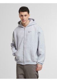 Grå zip-up hettegenser laget av mykt stoff, med en frontlomme, ribbede ermer og hette med snøring. Lite logo på brystet.