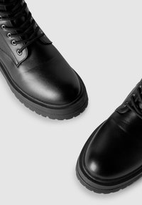 Czarne skórzane botki za kostkę z zaokrąglonym noskiem, solidną gumową podeszwą i sznurowaniem z metalowymi oczkami. Gładka tekstura z minimalnymi ozdobami.