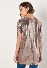 Top con lentejuelas en oro rosa, de corte suelto, mangas cortas y escote redondo. Textura suave con lentejuelas brillantes y reflectantes en toda la prenda.