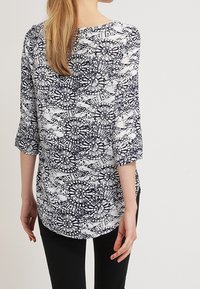 Long-sleeve, navy and white patterned blouse with rounded neckline, lightweight fabric, and three-quarter sleeves. Elegant floral design.
