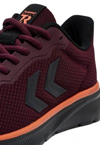 Chaussure de sport bordeaux avec une tige en mesh, accents noirs et détails orange. Présente une semelle texturée et des éléments de logo contrastants.