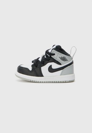 Black, white, and gray toddler sneaker with leather and synthetic upper, textured toe cap, black laces, and signature logo on the side.