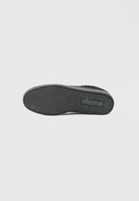 Mustmustel sneakeri põhi, millel on tekstureeritud pind geomeetrilise mustriga, mida täiendab sile vahekiht ja silt külgedel.