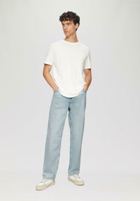Witte katoenen t-shirt met ronde hals, gecombineerd met lichtblauwe, losse spijkerbroeken en witte sneakers met beige accenten. Eenvoudige, casual outfit.