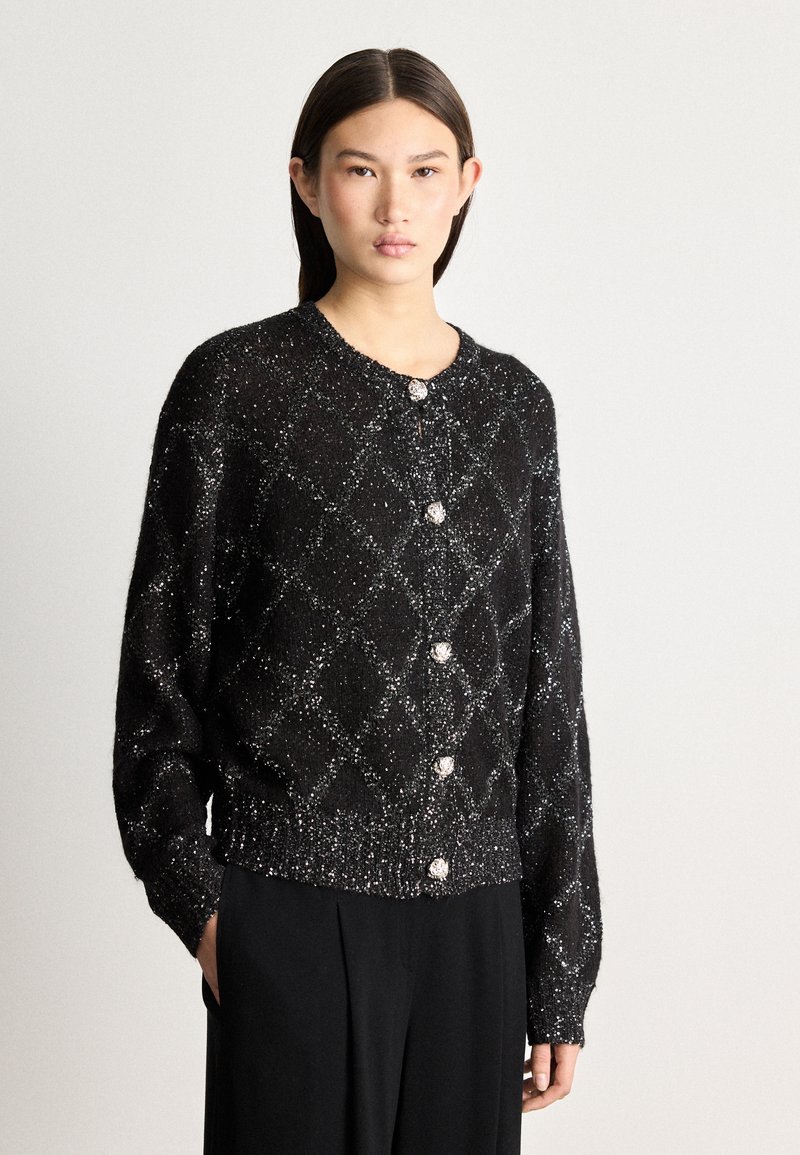 Black cardigan with diamond pattern in metallic thread, featuring round buttons and ribbed hem. Soft texture with long sleeves.