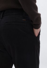 Juodos kelnės su tekstūruotu paviršiumi, turinčiomis galinę kišenę ir subtilų „BOSS“ logotipą. Audinys atrodo patvarus ir lygus.