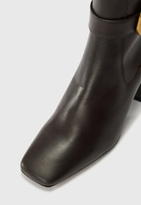 Brown leather ankle boot with a square toe and a low block heel, featuring a smooth texture and a side strap detail.