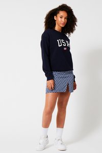 Navy sweatshirt with "USA" text and flag, paired with a patterned blue skirt featuring a front slit. White sneakers and socks complete the outfit.
