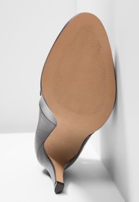 Musta korkeakorkoinen kenkä, jonka pinta on sileää nahkaa, kärki on terävä ja pohja kuvioitu. Korko on kapea ja kapeneva.