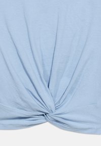 Ανοιχτό μπλε ύφασμα που έχει στριφτεί σε κόμπο στο κάτω κέντρο, δημιουργώντας συλλεγμένες πτυχές που ακτινοβολούν προς τα πάνω.