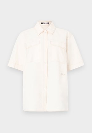 Camisa de manga curta, de cor creme, feita de tecido leve, com dois bolsos frontais, design com botões e costura em contraste.