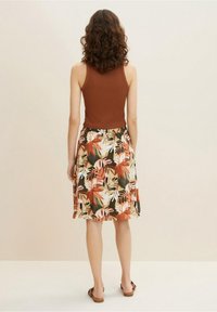 Débardeur marron à côtes associé à une jupe longueur genou avec un motif de feuilles tropicales colorées dans des teintes de vert, orange et crème.