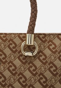 Brązowa torebka w wzory z plecionym uchwytem, złotymi akcentami i detalem z logo. Charakteryzuje się geometrycznym nadrukiem na trwałej powierzchni tkaniny.