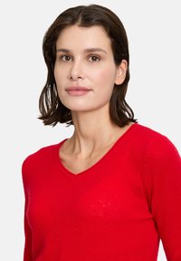 Pull rouge en V en tissu doux avec une finition légèrement texturée. Dispose de manches longues et d'une coupe ajustée pour un look épuré.