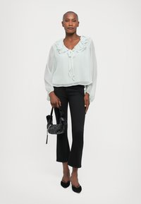 Light mint green blouse with ruffled neckline and bow, sheer long sleeves. Paired with black flared jeans and a black beaded handbag.