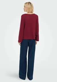 Maglione borgogna a trama con maniche lunghe, abbinato a jeans scuri a vita alta con gamba larga e orlo risvoltato.