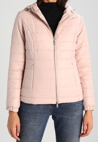 Giacca imbottita rosa chiaro con cappuccio, chiusura a zip frontale e polsini a costine. Presenta cuciture orizzontali e due tasche laterali.