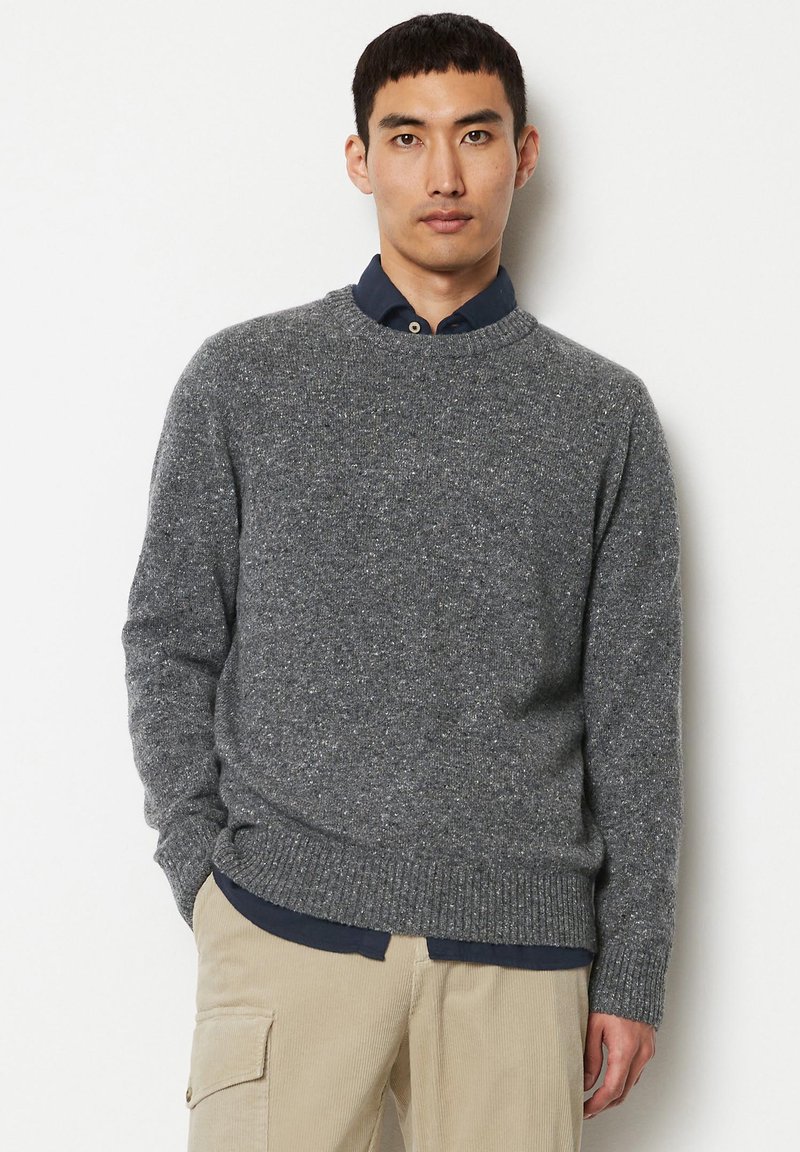 Grau gestrickter Pullover mit Rundhals, strukturiertem Stoff und gerippten Bündchen. Über einem blauen Hemd mit Kragen getragen, kombiniert mit beigen Hosen.