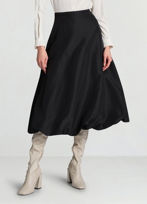 Jupe noire trapèze avec une texture lisse, longueur genou, associée à des bottes beige montantes à talon bloc et avec une fermeture éclair latérale.