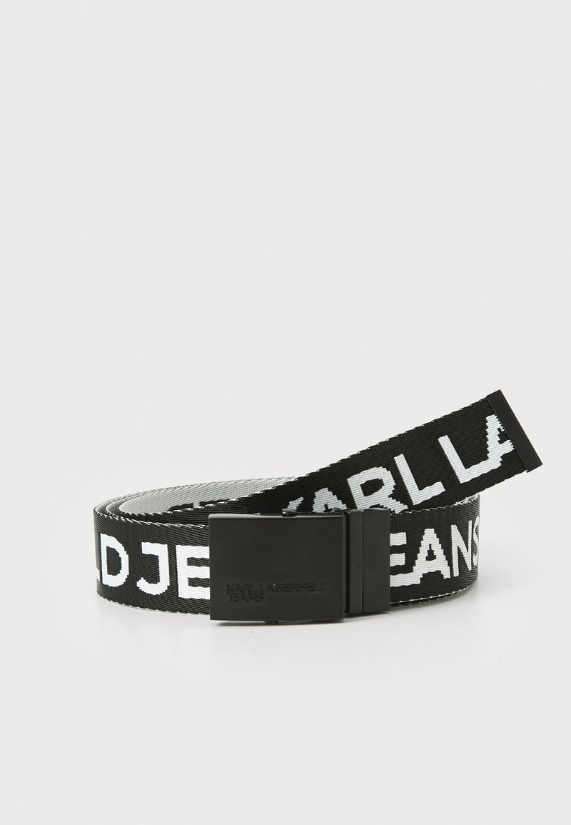 Svart og hvit nylonbelte med preget svart metallspenne. Har fet tekstmønster "KARL LAGERFELD JEANS" langs stroppen.
