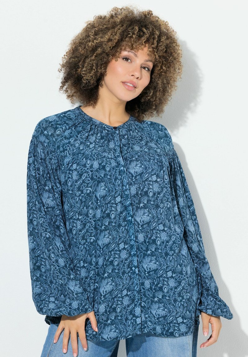 Blusa a maniche lunghe con motivo floreale blu, chiusure a bottoni e scollo arricciato. Realizzata in un tessuto morbido con una vestibilità comoda.