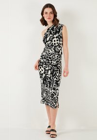 One-shoulder black and white dress with a fitted silhouette, featuring an intricate pattern and side slit. Worn with black strappy sandals.