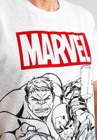 T-shirt in cotone grigio con un audace logo rosso "MARVEL" e illustrazioni in stile fumetto di personaggi, tra cui Hulk e Capitan America.