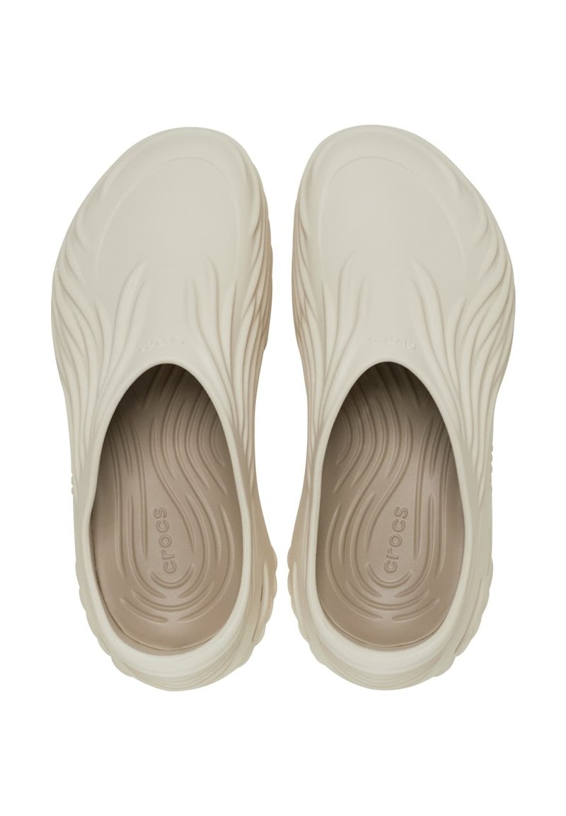 Crocs beiges avec une tige texturée ondulée, design à enfiler et intérieur rembourré. Matériau léger avec un logo discret sur la semelle intérieure.