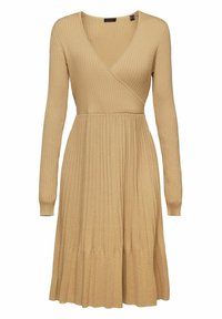Knitklänning i en ljusbeige nyans med V-ringning. Har långa ärmar, ribbad textur och en veckad kjoldesign.