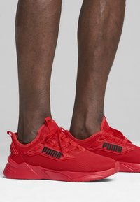 Zapatillas deportivas rojas con parte superior de malla, suelas texturizadas y marca PUMA negra. Diseñadas para comodidad y rendimiento, con un perfil aerodinámico.