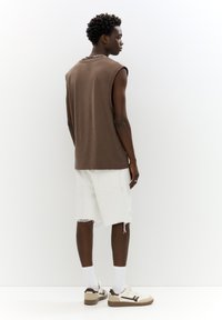 Brown sleeveless t-shirt, white distressed shorts, brown and cream sneakers, and white socks; shown from behind against a light background.