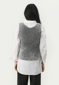 Grijze gebreide vest met een zachte, pluizige textuur, met een mouwloos ontwerp en ronde halslijn, gedragen over een wit shirt.