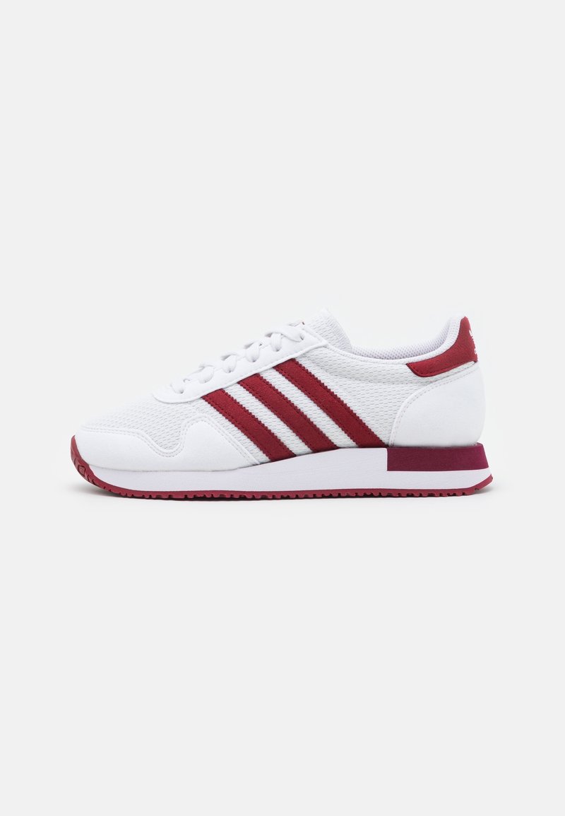 White athletic shoes with red accents and three red stripes. Textured mesh upper and rubber sole with a pinkish hue. Classic sneaker design.
